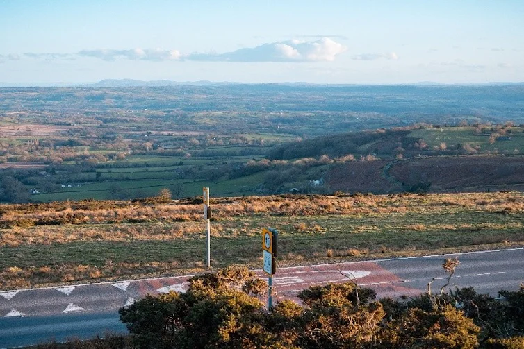 View Of Rolling Shropshire Countryside, Fields And Hills With A Road Visible In The Foreground Under The Cloudy Sky.